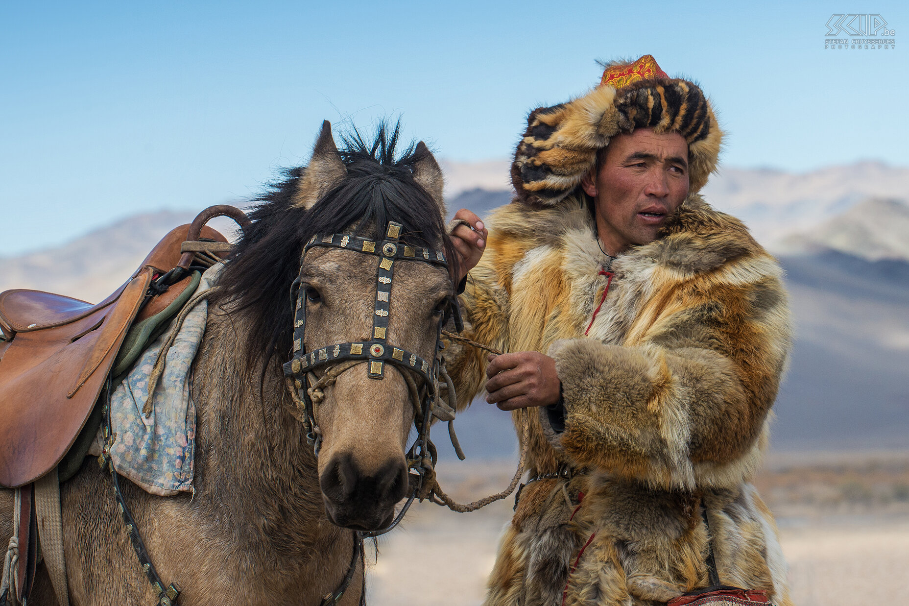 Ulgii - Golden Eagle Festival - Bontjassen De berkutchi dragen meestal hun traditionele klederdracht. Hun bontjassen zijn gemaakt van marmot, vos of wolf huiden die gevangen werden door hun adelaars. Hoe meer extravagant de uitrusting, hoe meer respect de jager krijgt. In het verleden waren deze bontjassen noodzakelijk en de beste bescherming tijdens de strenge winters in het Altai gebergte. De typische bonten muts wordt een 'tomach' genoemd. Stefan Cruysberghs